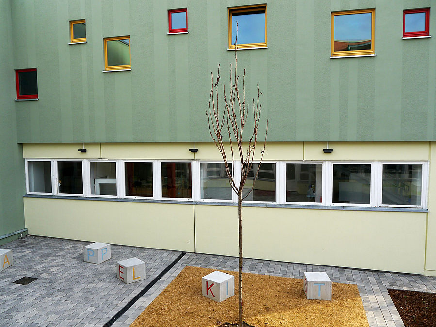 Fassade mit hellgelbem Erdgeschoss und grünem Obergeschoss mit unregelmäßigem Fensterband und farbigen Rahmen
