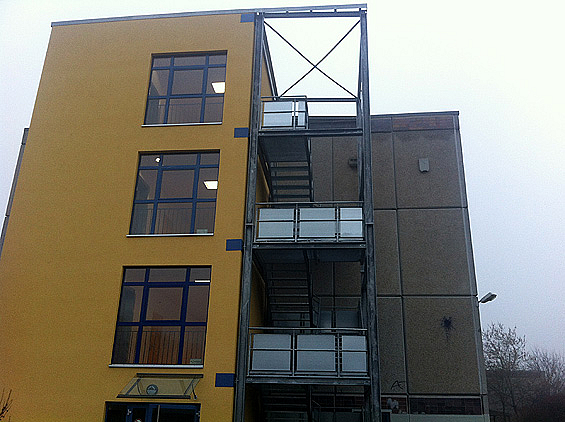 Gelber Anbau mit Fenstern, daneben Außentreppe aus Stahl mit Plattformen