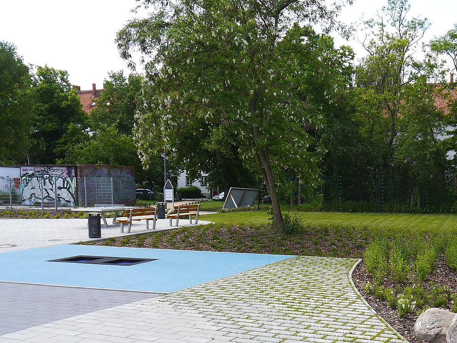 Trampolin in blauer Fläche, Rasenpflaster, Beete, Tischtennisplatte, Bäume