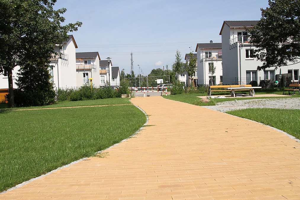 Breiter, gelber Plattenweg, Rasen, im Hintergrund Einfamilienhäuser