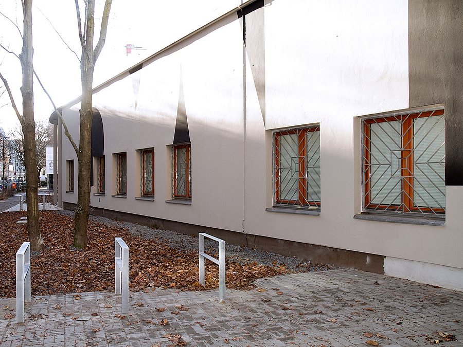 Helle Fassade mit schwazen geometrischen Formen, Eingang mit Farradbügeln