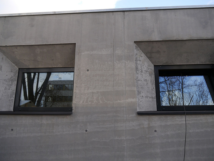 Zwei Fenster mit breiter Leibung und Brüstung auf grau-streifiger Betonwand