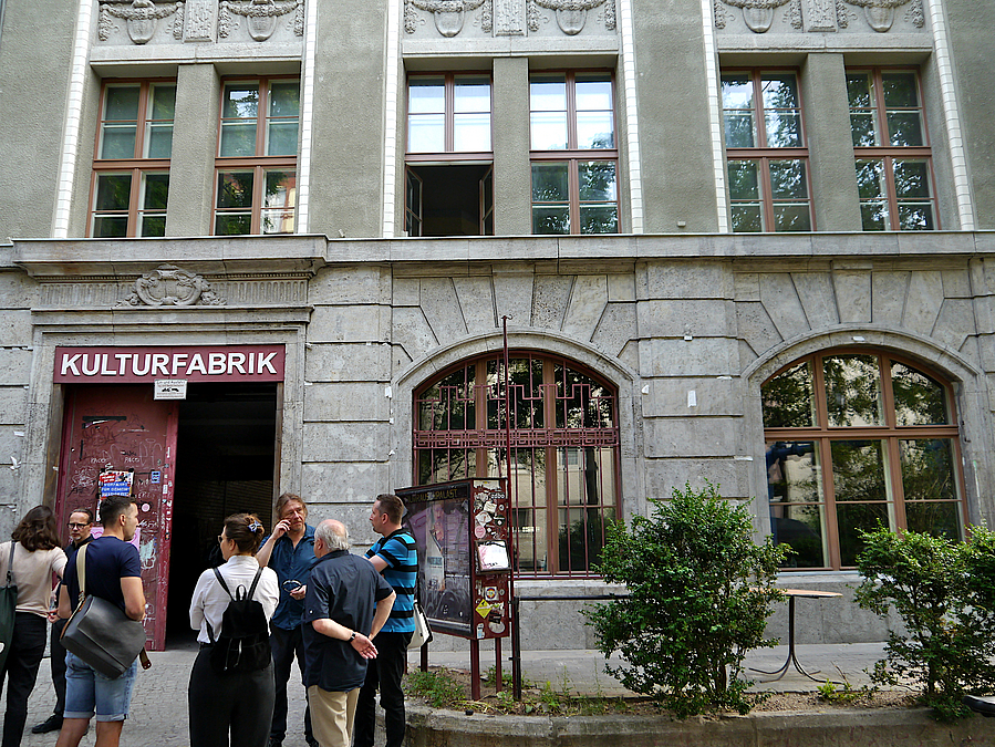 Altes Gebäude mit Aufschrift "Kulturfabrik" über rotem Tor, Menschengruppe