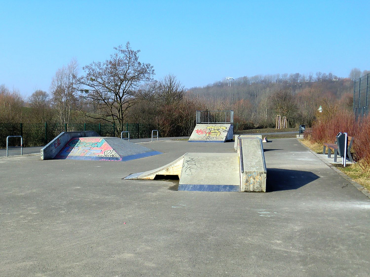 Skateanlage mit Hindernissen, vor bewaldetem Hügel im Frühling