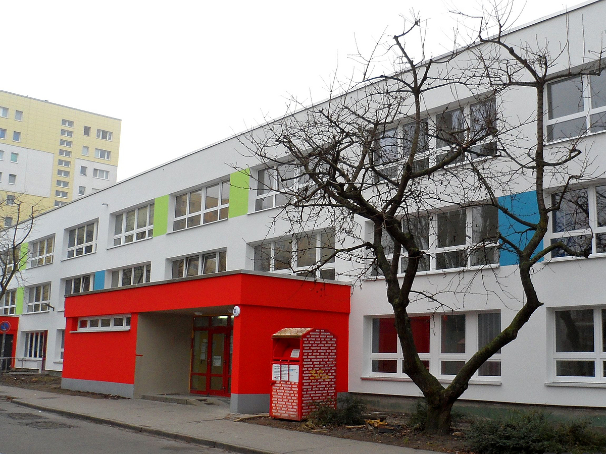 Kitatypenbau mit heller Fassade, hellgrüne und blaue Akzente, roter Eingangsbau