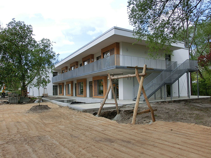 Zweigeschossiger Bau mit Flachdach und umlaufendem Balkon auf planierter Sandfläche