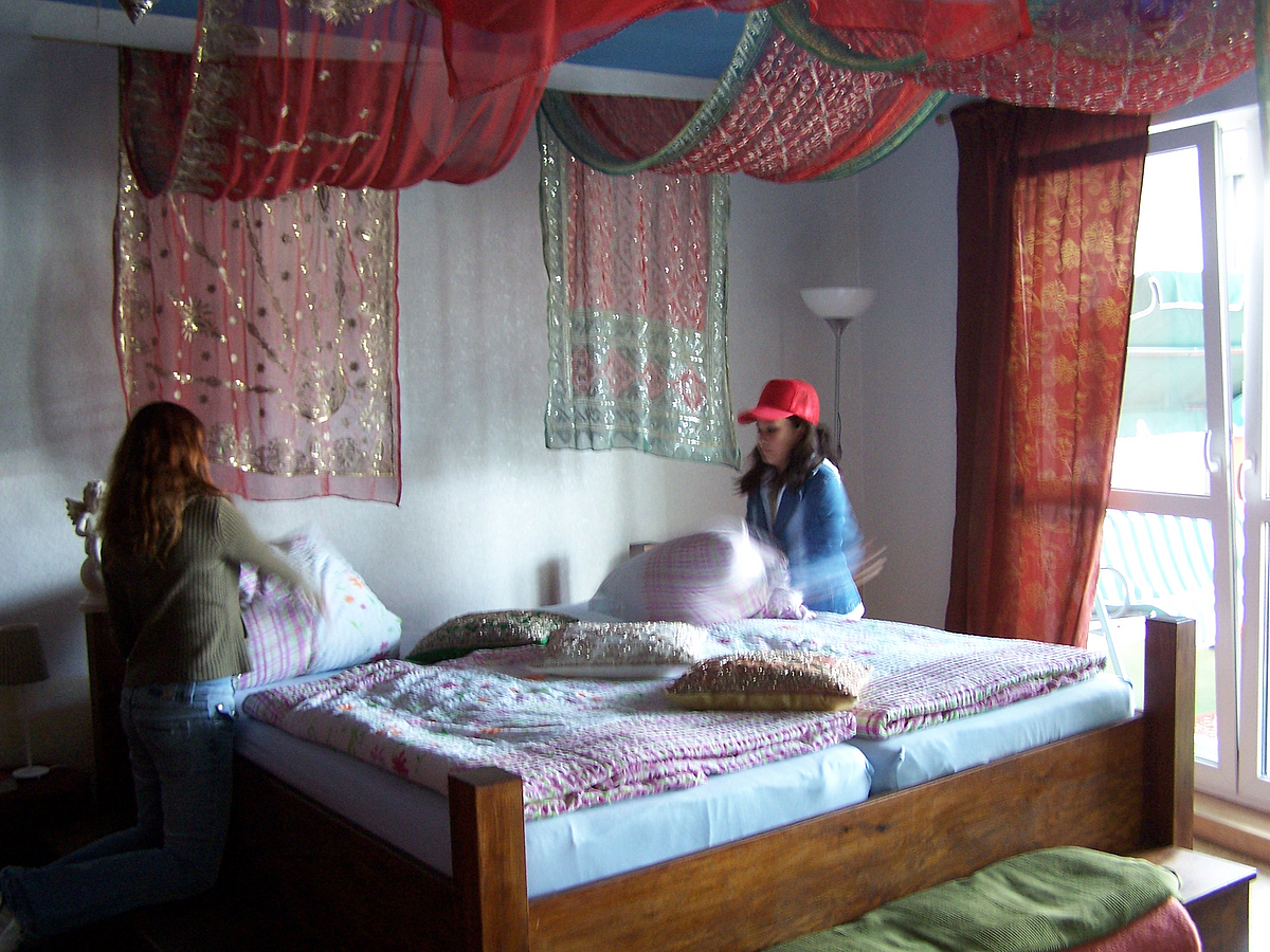 2 Mädchen klopfen Kissen eines Doppelbetts mit rotem Himmel