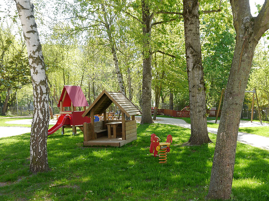 Kreines Rutschenhaus, Federwipptier und Hütte auf Rasen zwischen Bäumen