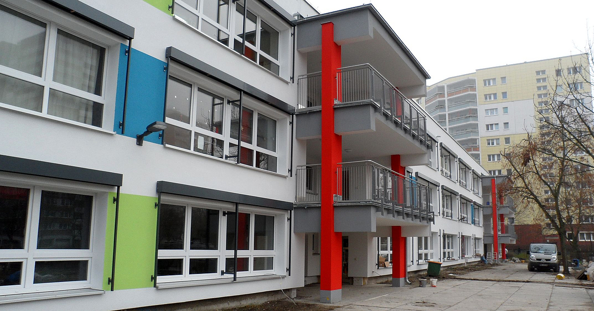 Kitatypenbau mit heller Fassade, rote, hellgrüne und blaue Akzente