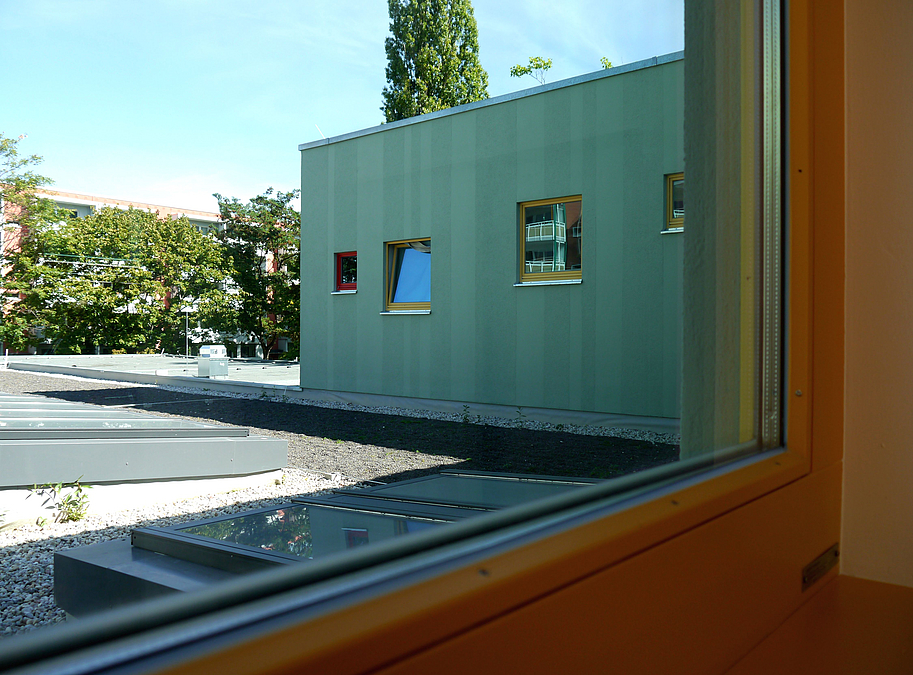 Blick durch Fenster auf Kiesbett und grüne Wand mit kleinen Fenstern