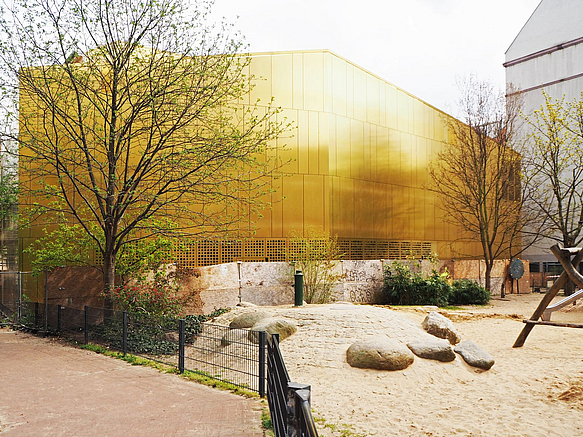 Golden glänzender, fensterloster Baukörper hinter Spielplatz
