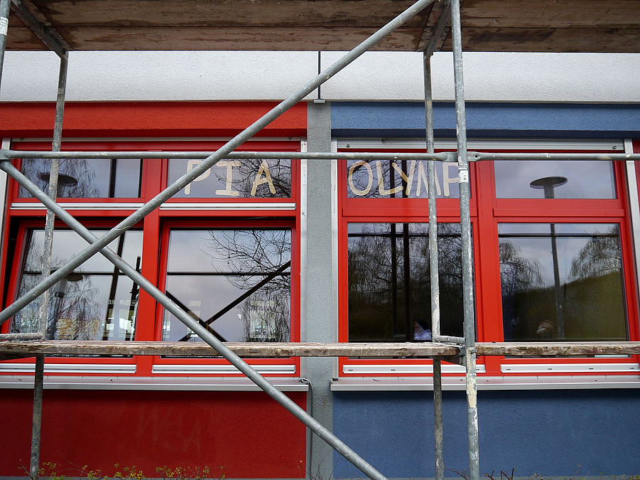 Detail vom Gerüst vor roter und blauer Fassade, Fenster mit Schriftzug "Pia Olymp"