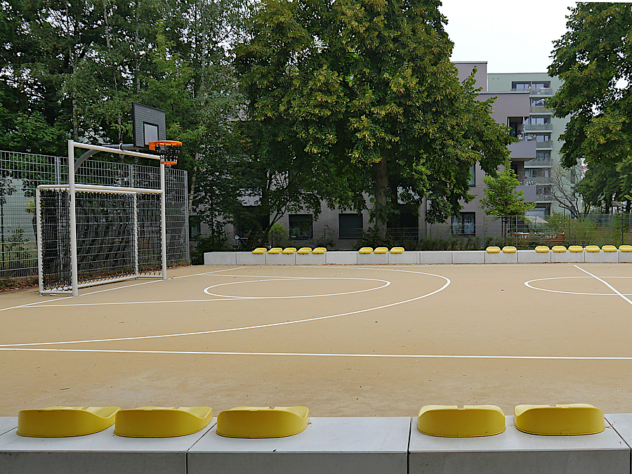 Bolzplatz mit hellem Boden und gelben Sitzen auf der betineinfassung