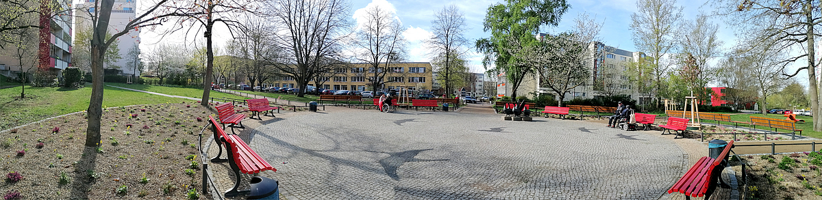Runder Platz mit ringsum aufgestellten roten Bänken im Grünen