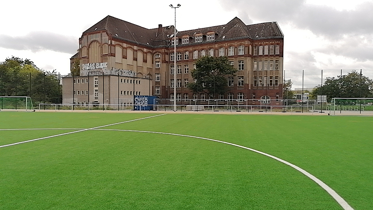Blick über Fußballplatz auf zweiflügliges, altes Schulgebäude