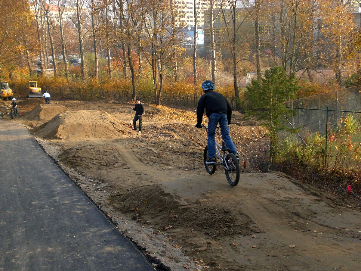 2 BMX-Fahrer auf hügeliger Piste neben Asphaltweg