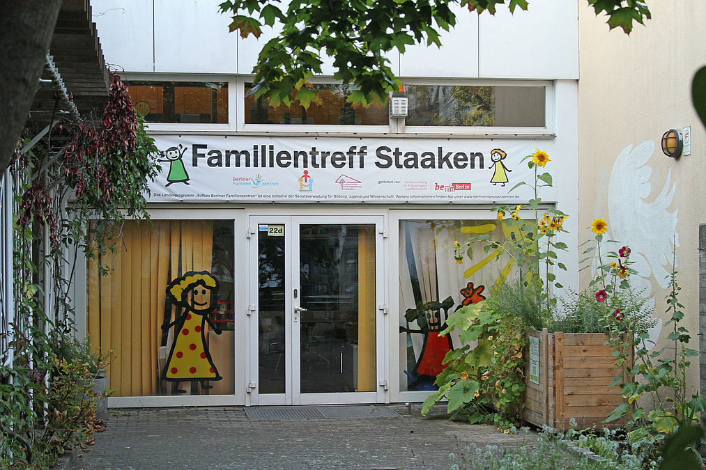 Eingang mit Fensterbildern und Banner "Familientreff Staaken", davor Kistenbeete, Sonnenblumen