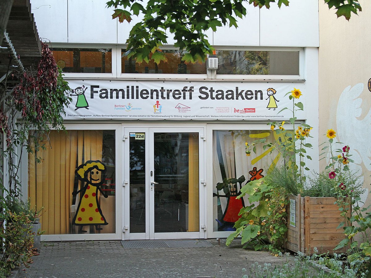 Eingang mit Fensterbildern und Banner "Familientreff Staaken", davor Kistenbeete, Sonnenblumen