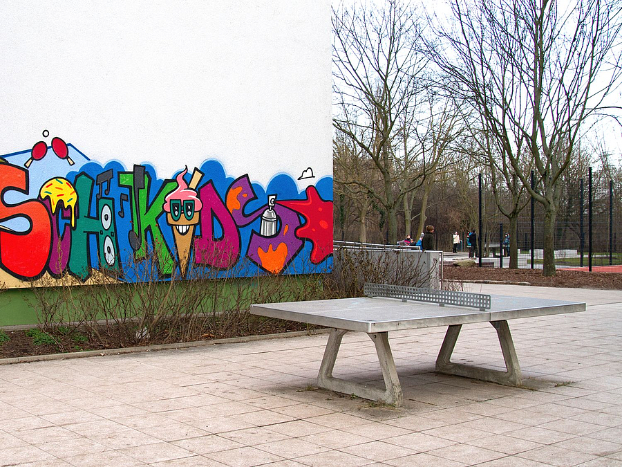 Tischtennisplatte vor Gebäudewand mit gestaltetem Graffiti-Schriftzug der Busch-Kids