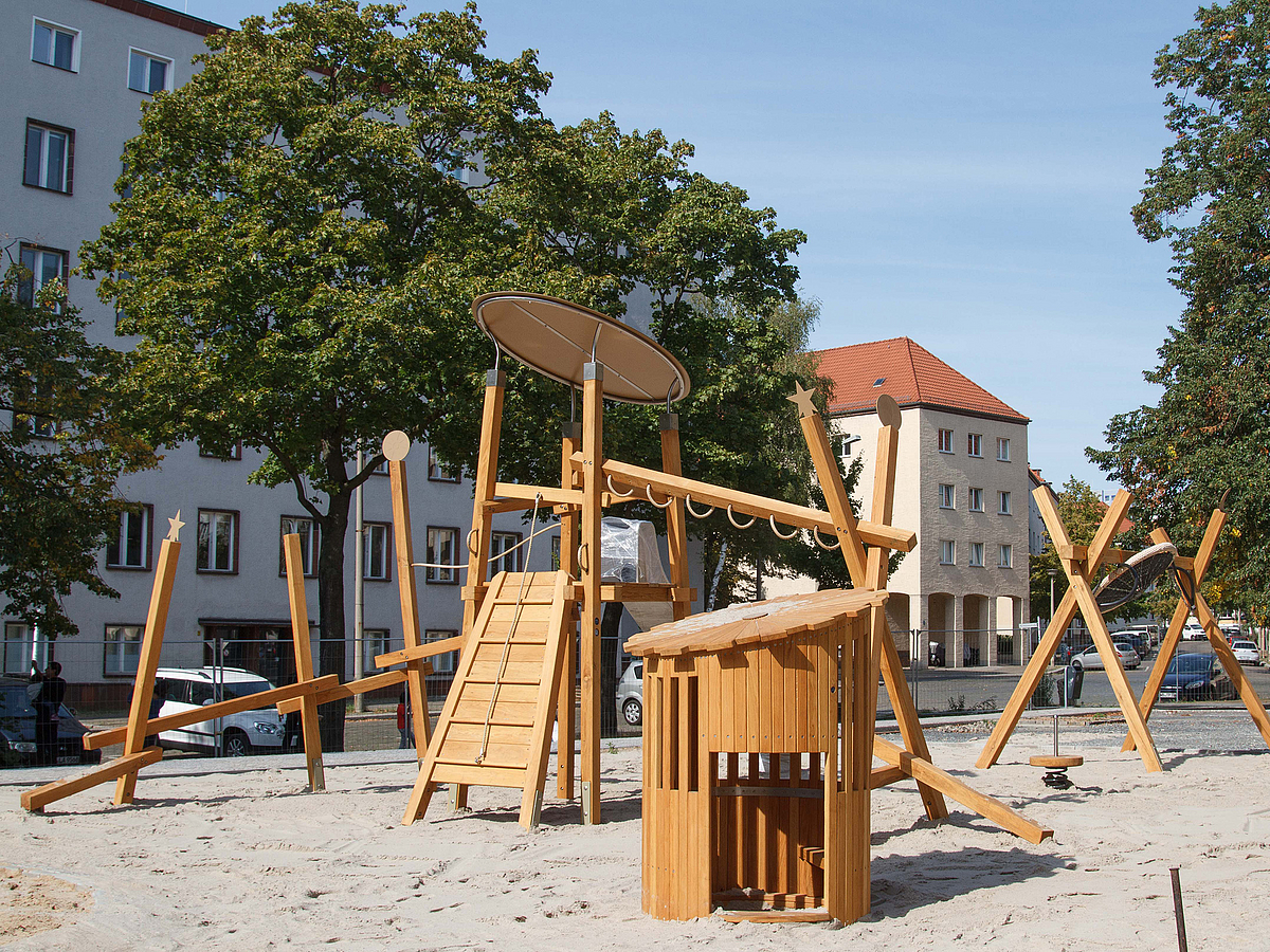 Spielplatz auf Sand mit Geräten aus Holz, Bäume, Wohnstraße