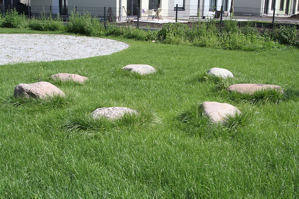 Kreis aus Findlingen im Rasen, daneben runde Pflasterfläche