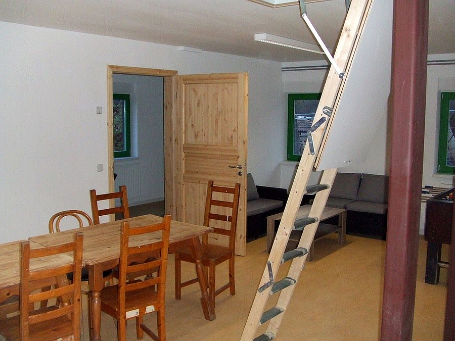 Raum mit Dachbodenleiter und rustikaler Einrichtung - Tische, Sofa, Holztür