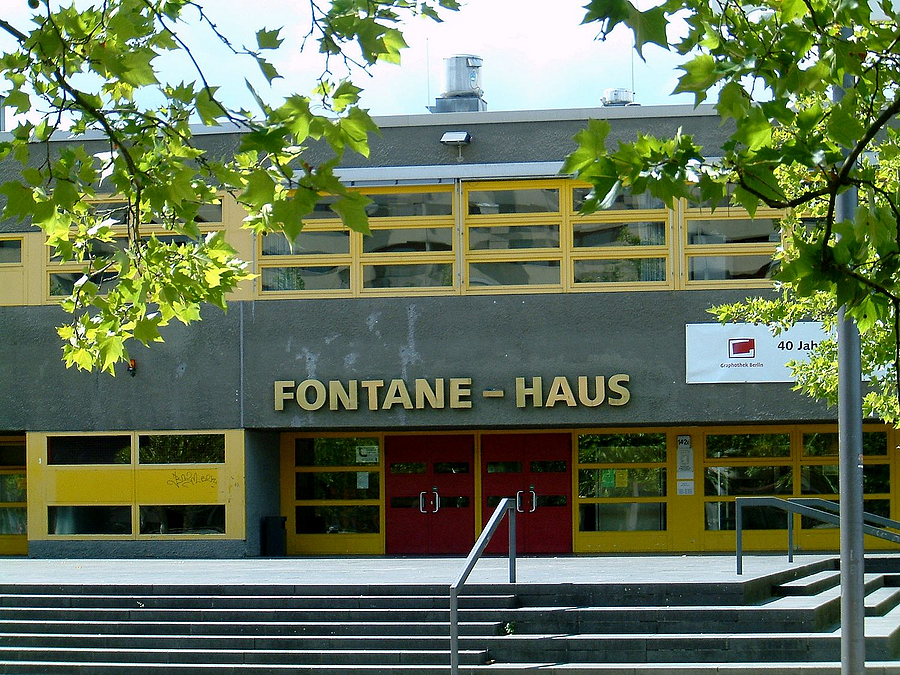 Grauer Zweigeschosser mit gelben Stahlrahmen der Fenster, Eingang Schriftzug Fontane-Haus