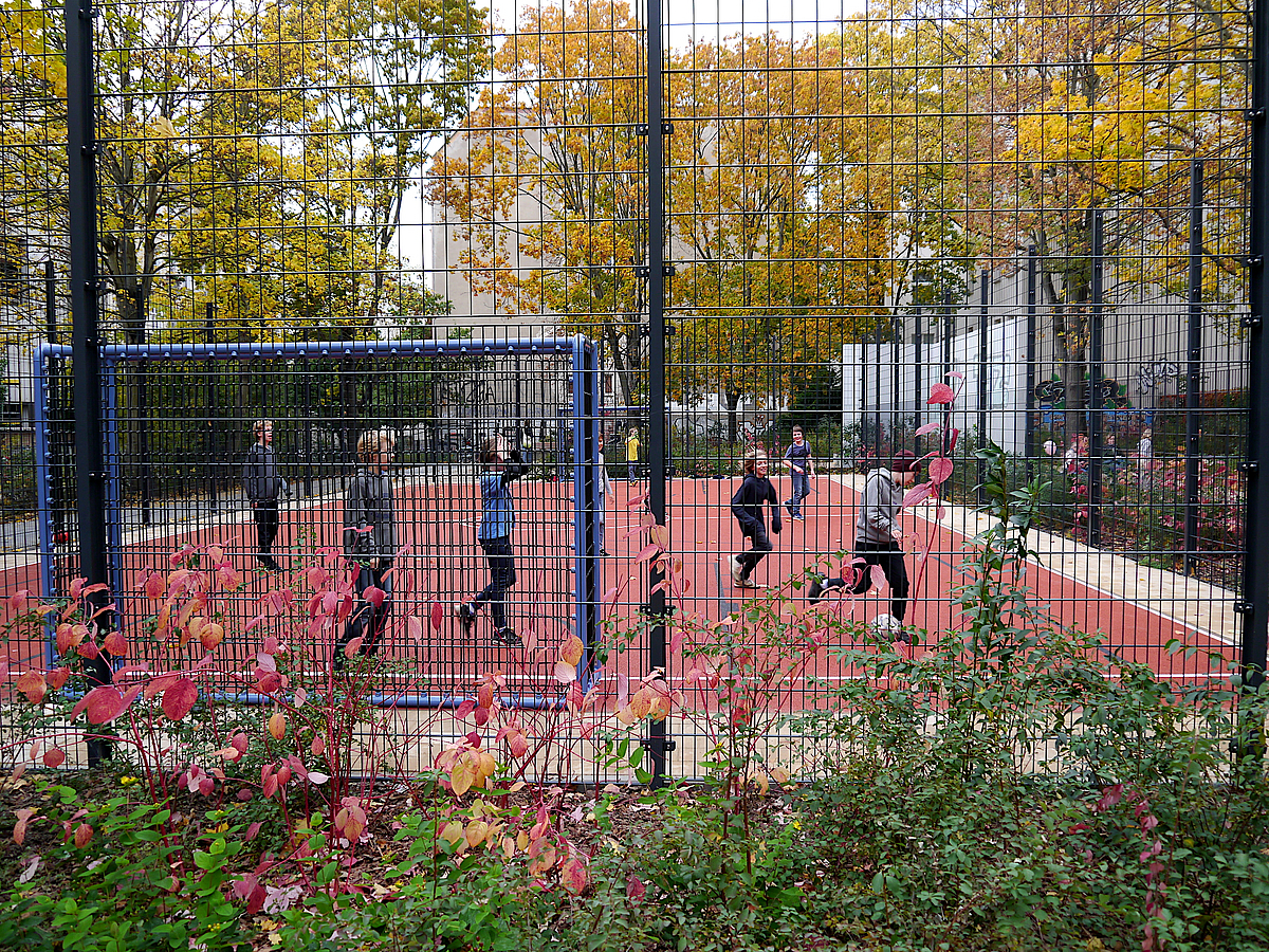 Bolzplatz in rot mit Ballfangzaun und Umpflanzung, Kinder