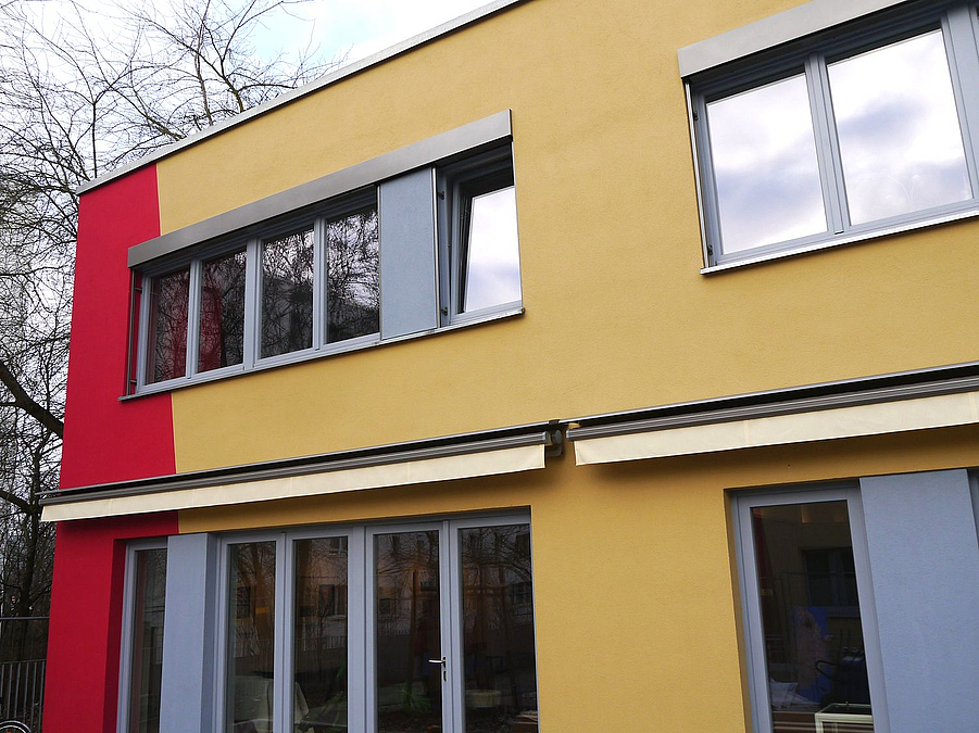 Gelb-rote Fassade mit blaugrauen Fenster- und Türrahmen