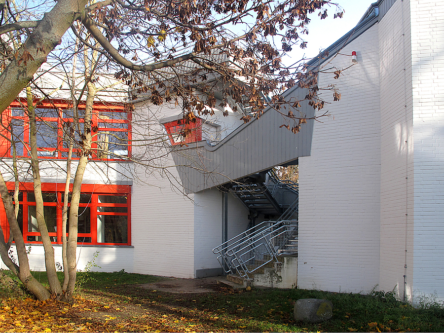 Mehrtgeiliger, zweigeschossiger Klinkerbau in Weiß mit roten Akzenten, gewinkelte Stahltreppe eingepasst zwischen zwei Gebäudeteilen