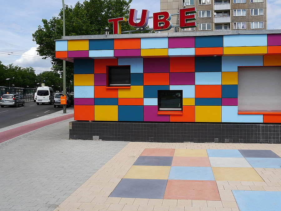 Kiosk mit Verkleidung aus bunten Platten, davor gleichfarbige Bodenplatten