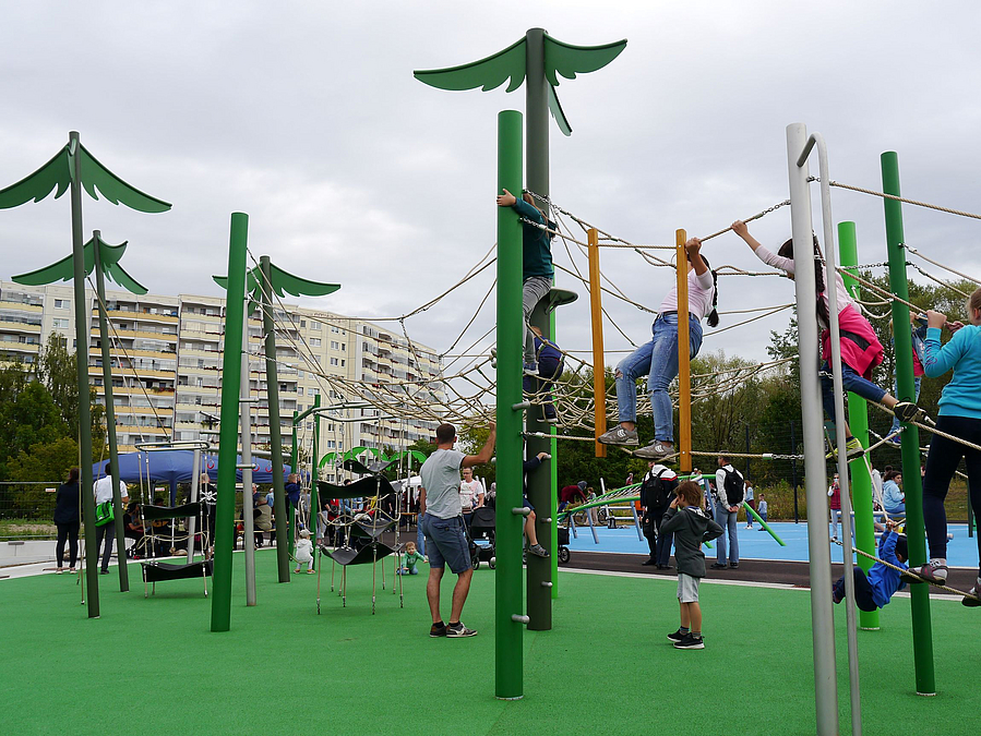 Holzmasten als Bäume mit dazwischen gespannten Seilen auf grünem Kunststoff, Eltern und Kinder
