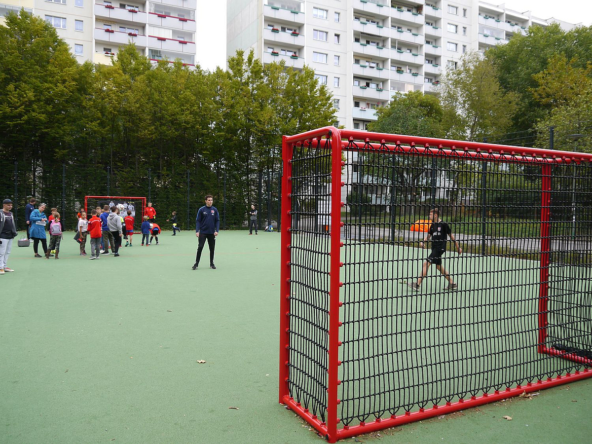 Bolzplatz mit grünem Kunststoffboden und roten Fußballtoren, Spielende