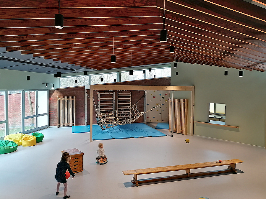 Saal mit Zeltdach und gefalteter Holzdecke, Kletterwand, Turnbank, Sitzsaecke, 2 Kinder