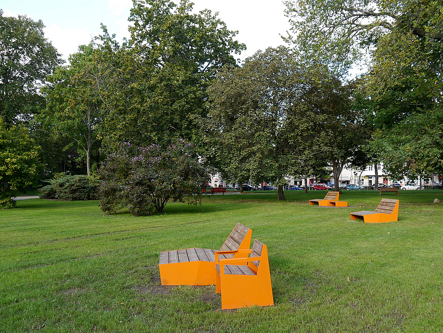 Wiese, große Bäume, orangefarbene Sitzmöbel