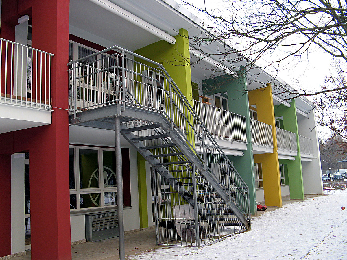 Laubengang eines zweistöckigen Gebäudes, farbige Trennwände, Außentreppe aus Stahl