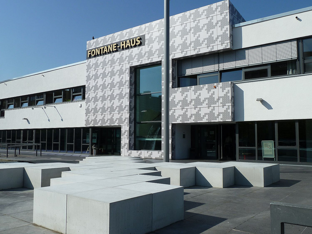 Modernes Gebäude mit stilisierten F als Portal und Schrift "Fontane-Haus", davor Platz mit Betonquadern