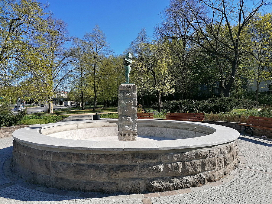 Runder Brunnen mit Knabenfigur auf Sockel im Park
