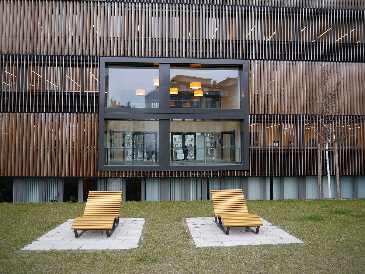 Fassade aus Holzlamellen, davor 2 Liegestühle auf Rasen