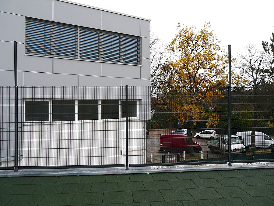 Blick von eingezäunter Terrasse auf 2 Obergeschosse in Grau und Weiß mit Fensterbändern