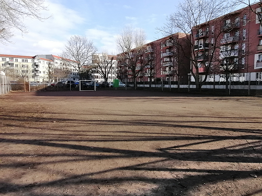 Große, unbefestigte Fläche im Winter, Wohnbebauung, im Hintergrund Fußballtor
