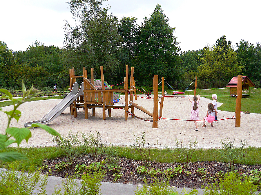 Spielplatz mit Kindern auf San, Pflanzfläche, Sträucher im Vordergrund