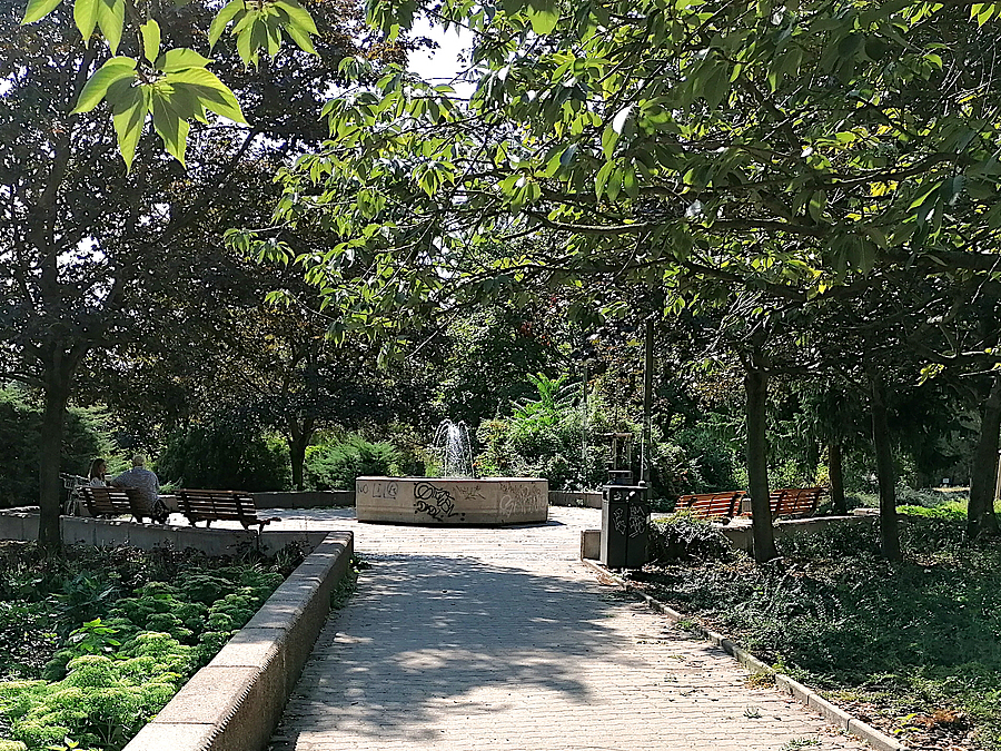Weg zwischen Laubbäumen, im Hintergrund Springbrunnen