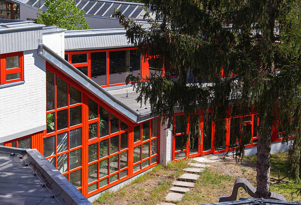 Blick von oben auf kleinteilig rot gegliederte Glasfassade eines abgeschrägten Vorbaus