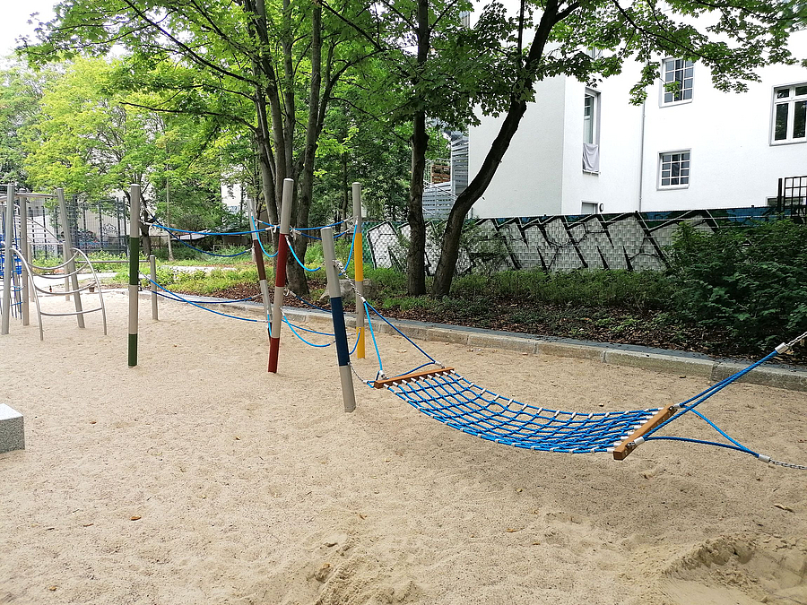 Sandfläche mit Hängematte und niedrigem Kletterparcours aus Metall, Seil, Holz