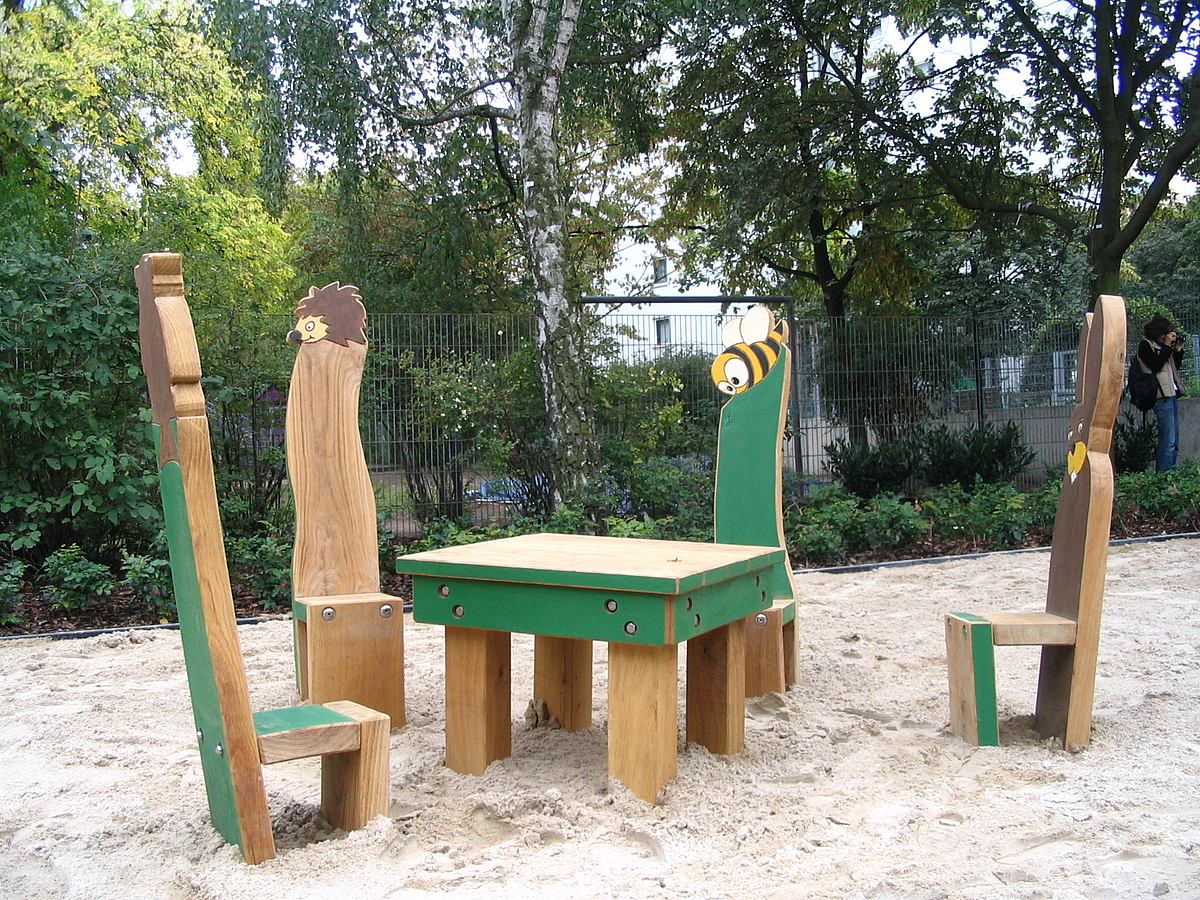 Sitzgruppe aus Holz im Sand, Stühle mit hohen Lehnen mit Abschluss Tierfiguren