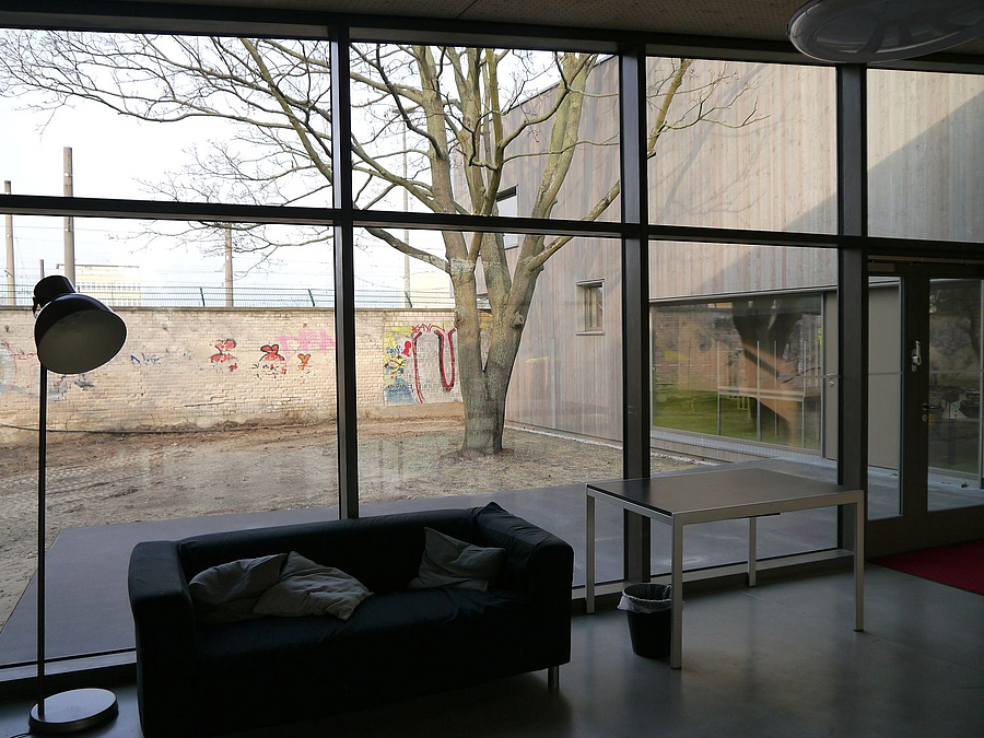 Innenraum mit Möbeln vor Glasfront mit Blick auf Baum, Seitefklügel u. Mauer