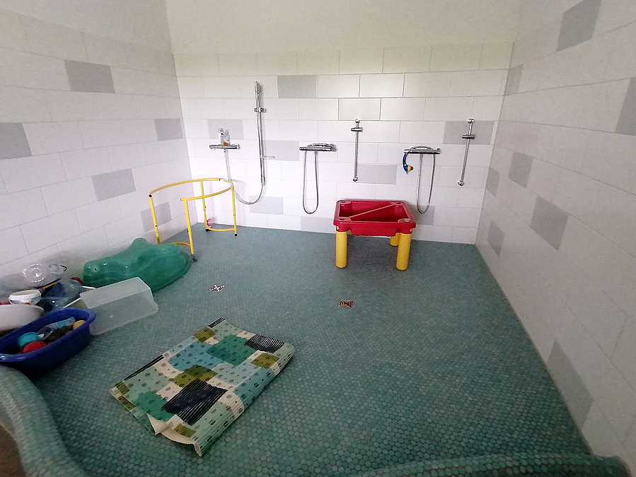 Gekachelter Raum mit blauem Mosiakfußboden, 6 Duscharmaturen, Matten und Wasserspielzeug