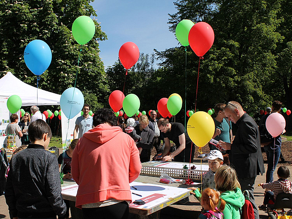 Menschen an Tischtennisplatte im Freien, darüber Luftballons an Schnüren