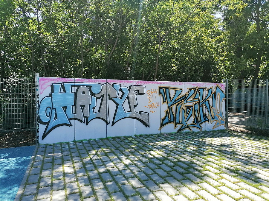 Mauerteile vor Bäumen mit Graffiti-Schriftzügen